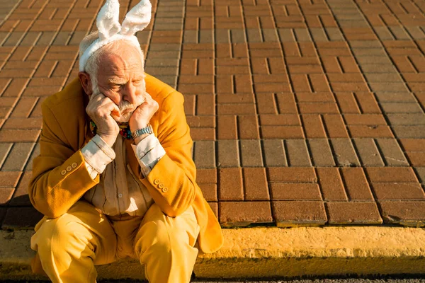 Αναστατωμένος ηλικιωμένος άνδρας με κίτρινο κοστούμι κάθεται στο δρόμο στην πόλη — Φωτογραφία Αρχείου