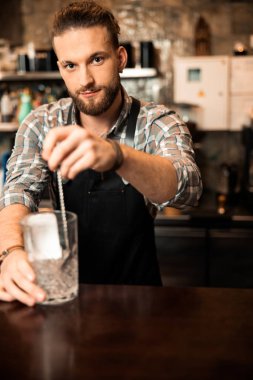 Sakallı barmen, buz küpleriyle alkol karıştırıyor.