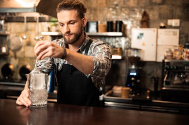 Barmen sakallı, bardakta alkol karıştırıyor.