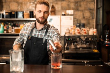 Genç sakallı barmen ölçü bardağı kullanıyor.