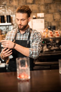 Genç sakallı barmen elinde bir şişe alkol tutuyor.