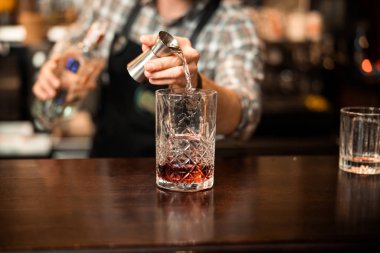 Barmen viski kokteyllerine kokteyl malzemesi ekliyor.