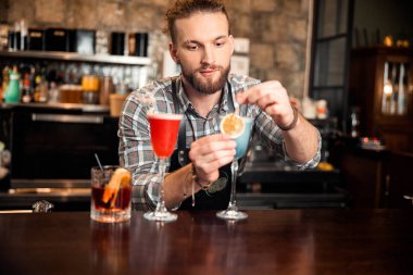 Barmen üç farklı kokteylin yanında duruyor.