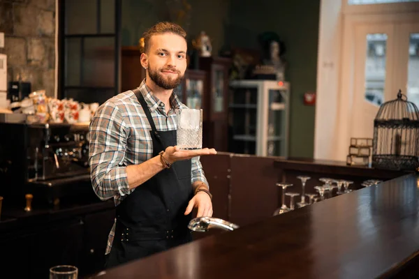 Улыбающийся бармен держит стекло со льдом — стоковое фото