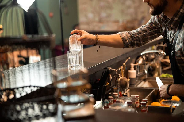 Barman z brodą wkłada lód do szklanki. — Zdjęcie stockowe
