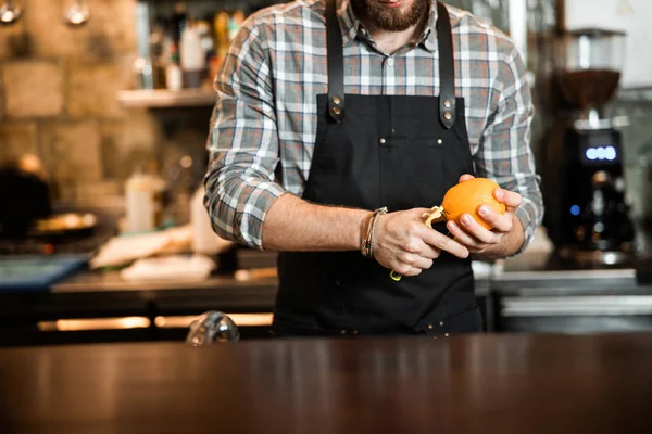 Молодой бармен чистит апельсин в баре — стоковое фото