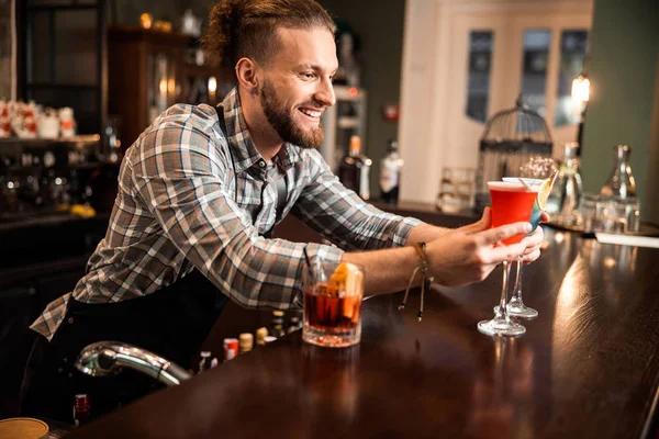 Счастливый бармен смотрит на два красочных коктейля — стоковое фото