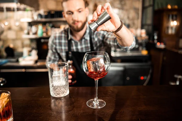 Joven barman vertiendo alcohol en un vaso con hielo — Foto de Stock