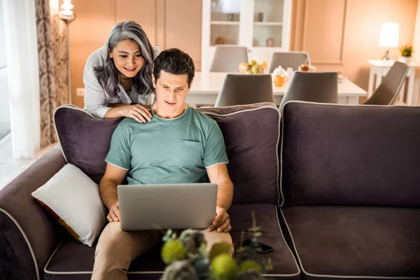 Feliz marido maduro com sua esposa usando laptop na sala de estar — Fotografia de Stock