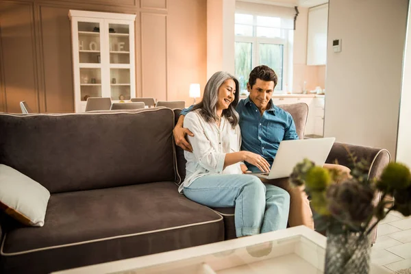 Glückliche erwachsene Frau tippt auf Laptop im Wohnzimmer — Stockfoto