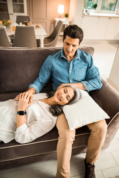 Uomo sorridente guardando sua moglie mentre riposava sul divano a casa — Foto Stock