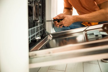 Close up of professional worker holding screwdriver to repair dishwasher