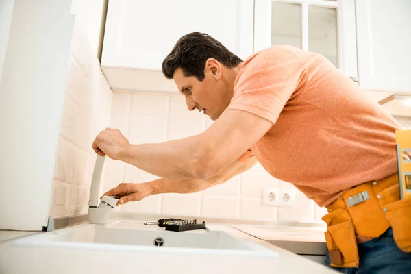 Erwachsener Arbeiter benutzt Schraubenzieher, während er Wasserhahn in der Küche repariert — Stockfoto