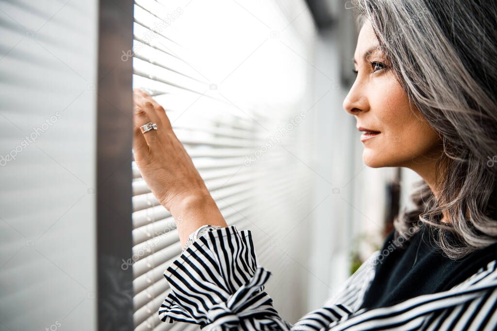 Thoughtful woman by the window peeking out stock photo