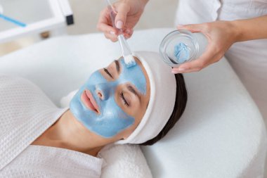 Güzellik uzmanı elleri kadının yüzüne kozmetik maske takıyor.
