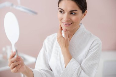 Güzel bayan yüzüne dokunuyor ve aynaya bakıyor.