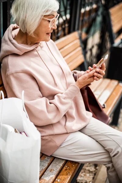 Mujer Seniour con teléfono inteligente en banco de fotos de stock — Foto de Stock
