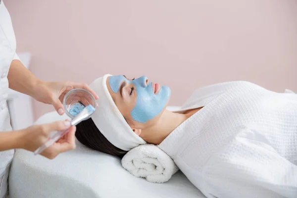 Esteticista aplicación de máscara cosmética en la cara de la mujer joven — Foto de Stock