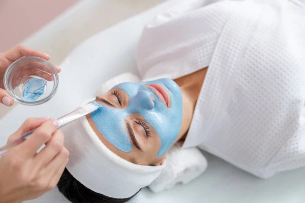 Esteticista aplicando máscara de barro azul no rosto da senhora — Fotografia de Stock