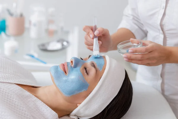 Esteticista aplicando máscara azul no rosto da mulher — Fotografia de Stock