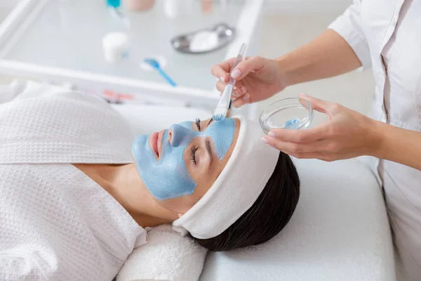 Esteticista feminina aplicando máscara cosmética no rosto da senhora — Fotografia de Stock