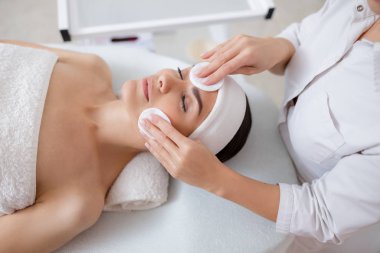 Güzellik uzmanı, pamuk pedlerle kadın yüzündeki kirliliği temizliyor.