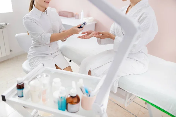 Cosmetologist sorridente que dá a nata cosmética à mulher jovem — Fotografia de Stock