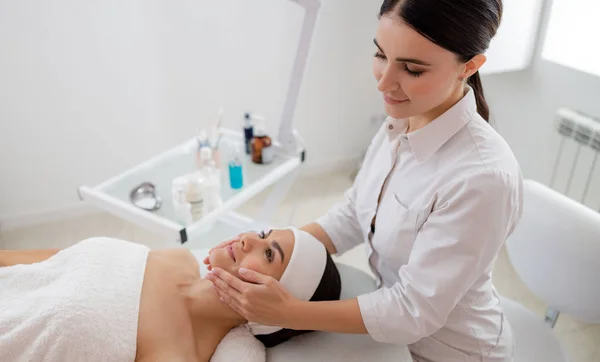 Sorridente massaggiatrice massaggio viso di giovane donna — Foto Stock