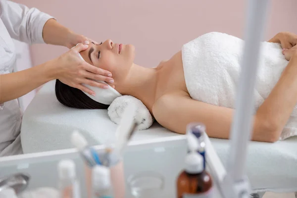 Mujer joven y relajada disfrutando de masajes faciales en el salón de spa — Foto de Stock