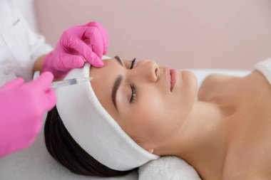 Kadın kozmetik uzmanı kadının alnına iğne yapıyor.