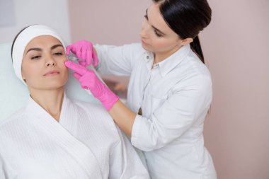 Güzellik uzmanı genç bir kadının yüzüne iğne yapıyor.