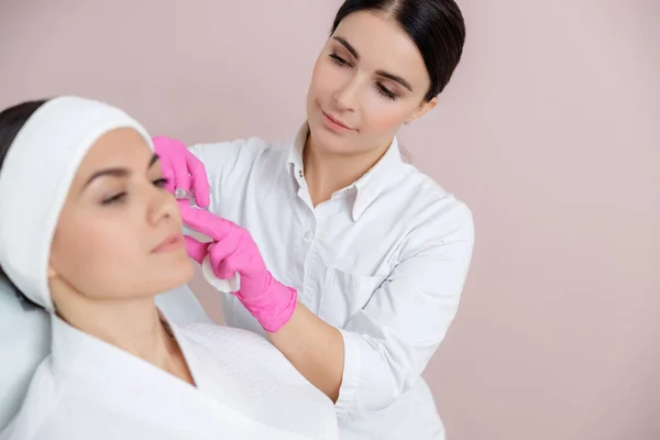 Lächelnde Kosmetikerin spritzt junger Frau Spritze ins Gesicht — Stockfoto