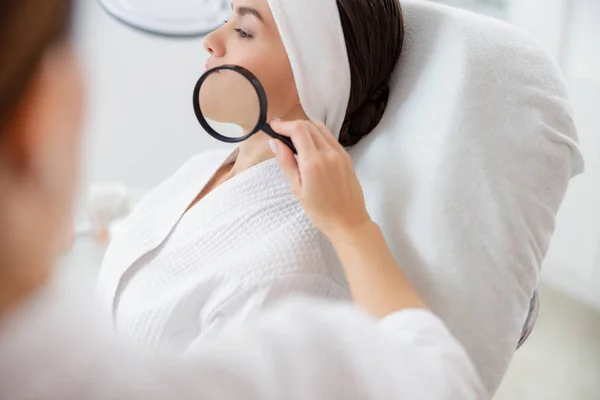 Cosmetólogo examinando la piel de la señora con lupa — Foto de Stock