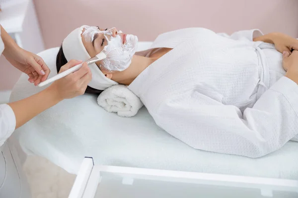 Güzellik uzmanı kadın yüzüne fırçayla kozmetik krem sürüyor. — Stok fotoğraf