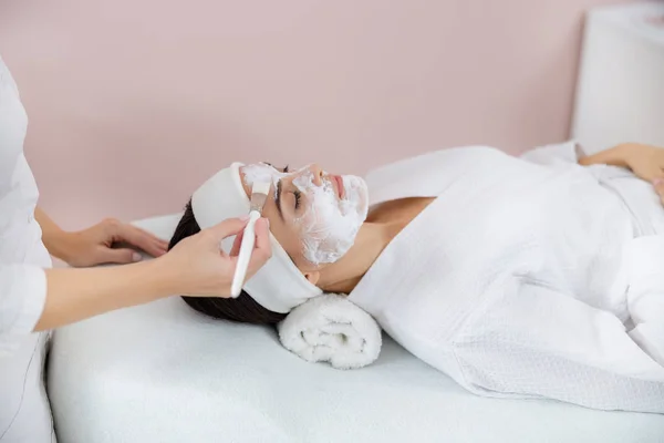Esteticista aplicando mascarilla cosmética purificante en la cara de la señora — Foto de Stock