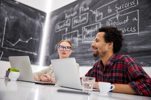 Sorridente giovane uomo e signora seduti a tavola al lavoro — Foto Stock