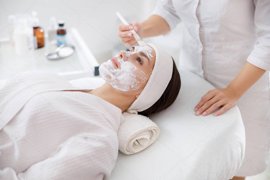 Beautician applying cosmetic mask on lady face