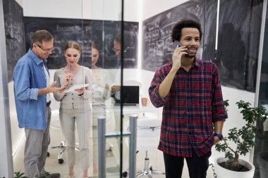 İş arkadaşları çalışırken gülümseyen adam cep telefonuyla konuşuyor.