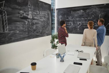 İş arkadaşları ofiste tahtanın önünde duruyorlar.