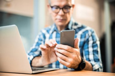 Yetişkin adam ofiste otururken akıllı telefon kullanıyor.