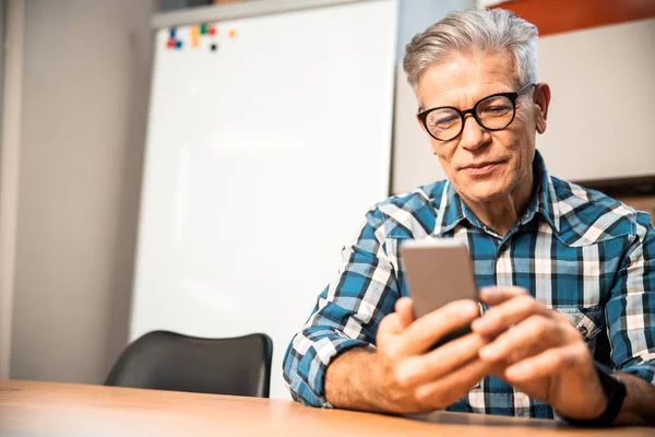 Leende vuxen man tittar på smartphone skärm på kontoret — Stockfoto