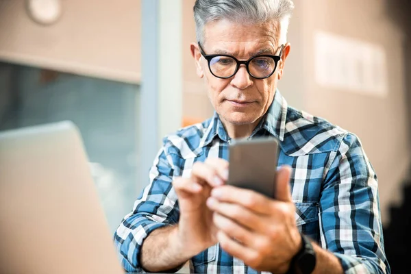 Mature man in glasses holding mobile phone in hands — Stock Photo, Image