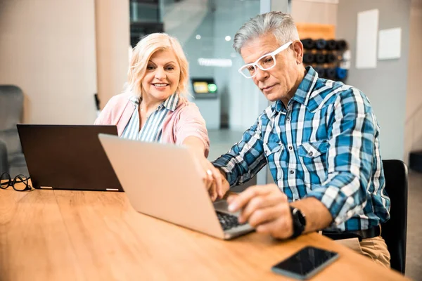 Glada mogna par som använder bärbara datorer på arbetsplatsen — Stockfoto