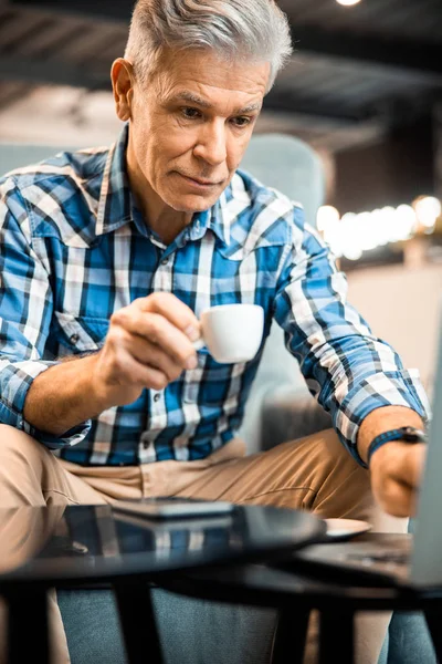 Усміхнений зрілий чоловік насолоджується гарячим напоєм у кафе — стокове фото