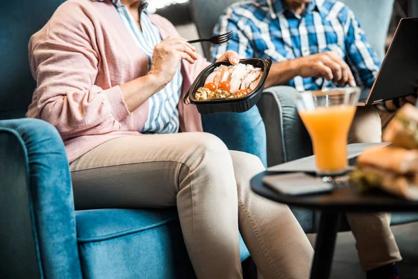 Gammal kvinna som håller mat sittande i fåtöljen — Stockfoto