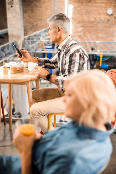 Vuxen gråhårig man som håller smartphone och dricker kaffe — Stockfoto