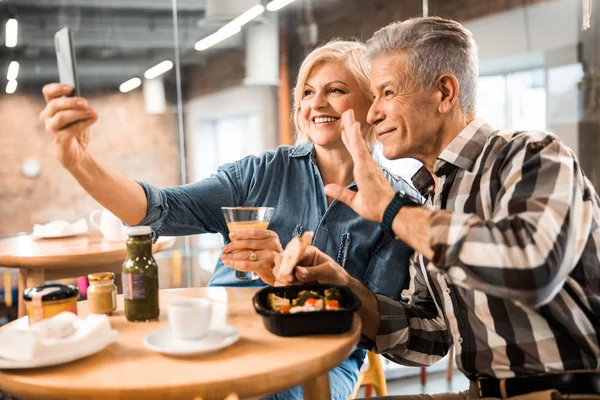 Feliz madura hombre y mujer mirando a la cámara del teléfono en la cafetería —  Fotos de Stock