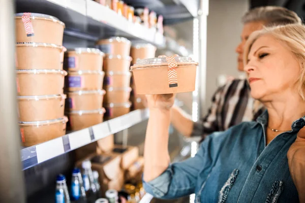 Femme mature tenant la boîte avec de la nourriture dans le magasin — Photo