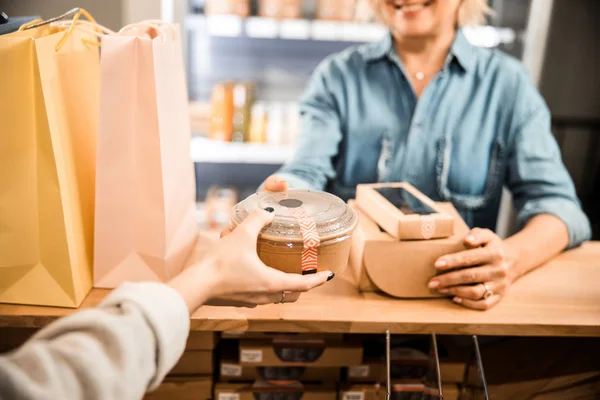 Leende kvinnlig shoppare ger matlåda till kassören i butiken — Stockfoto