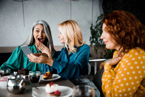 Lächelnde Dame zeigt Freundin etwas Aufregendes auf Handy — Stockfoto